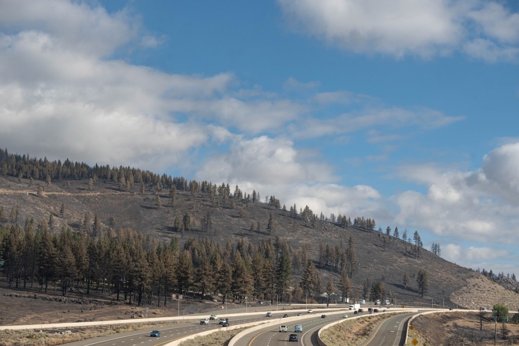 Cars drive on Highway 395 as the burn scar shows on the hill above the road